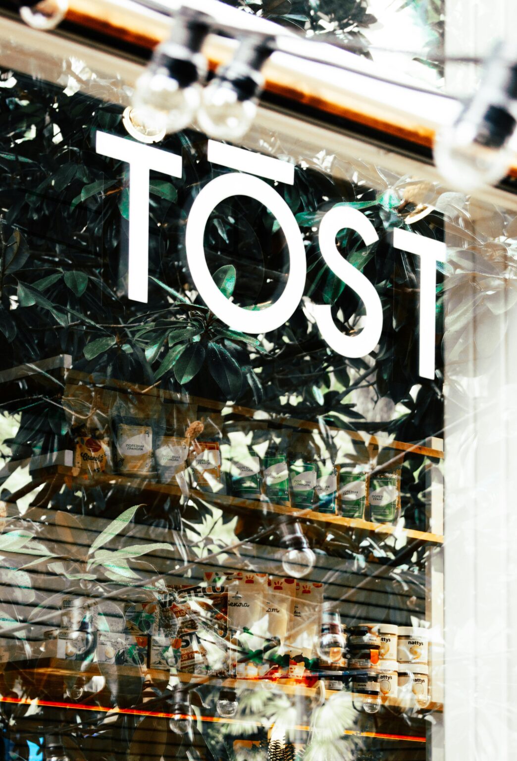 A modern urban storefront captured through a reflective glass window with leafy background.
