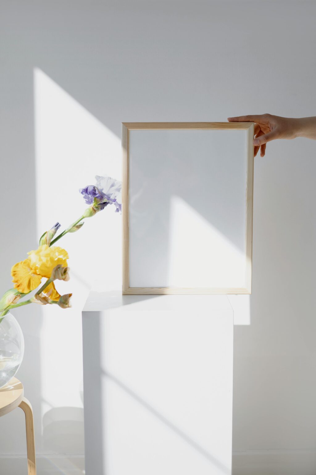 A minimalist mockup featuring a wooden frame held by a hand, with vibrant flowers in a Scandinavian-style interior.